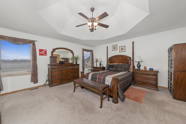 carpeted bedroom featuring multiple windows, a raised ceiling, and ceiling fan