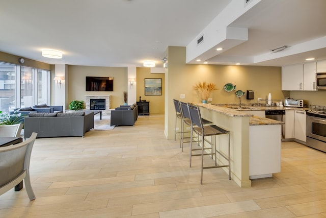 kitchen with white cabinetry, appliances with stainless steel finishes, a breakfast bar, and light stone countertops