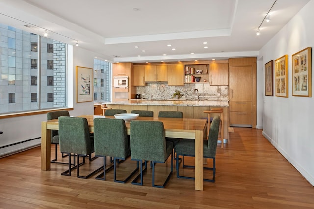 dining room featuring baseboard heating, a tray ceiling, light hardwood / wood-style flooring, and wet bar