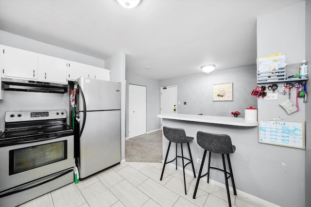 kitchen featuring a breakfast bar area, appliances with stainless steel finishes, white cabinetry, light colored carpet, and kitchen peninsula