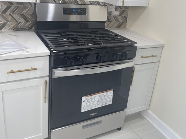 details featuring gas range, decorative backsplash, and white cabinets