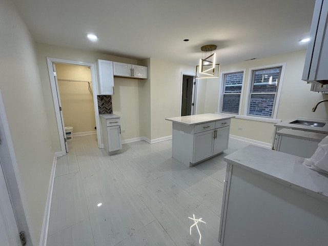 kitchen featuring hanging light fixtures, a kitchen island, sink, and white cabinets