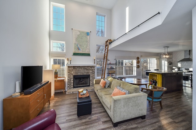 living room featuring dark wood-type flooring, an inviting chandelier, a brick fireplace, and a high ceiling