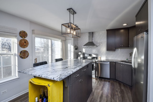 kitchen featuring appliances with stainless steel finishes, dark brown cabinets, decorative backsplash, and wall chimney exhaust hood