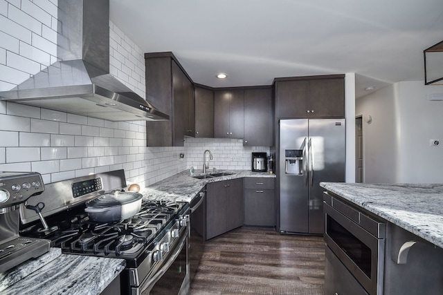 kitchen featuring wall chimney exhaust hood, dark brown cabinetry, sink, appliances with stainless steel finishes, and light stone countertops