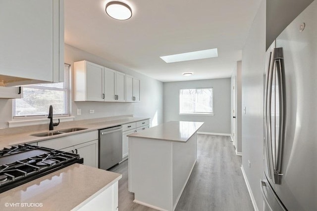 kitchen with sink, white cabinetry, a skylight, a center island, and stainless steel appliances