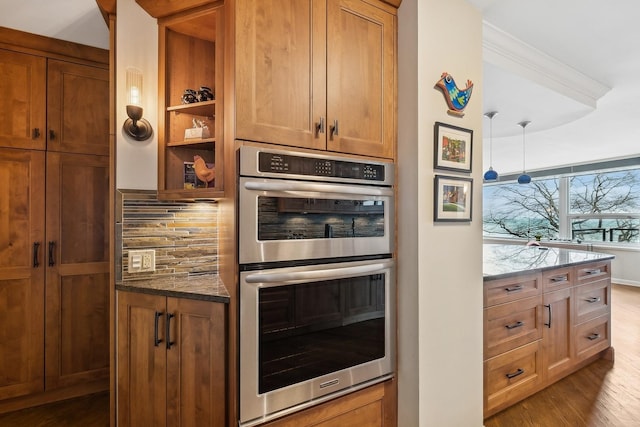 kitchen with light hardwood / wood-style flooring, dark stone countertops, hanging light fixtures, tasteful backsplash, and stainless steel double oven