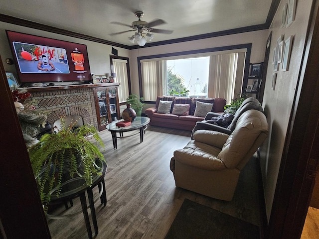 living room featuring wood-type flooring, a brick fireplace, ceiling fan, and crown molding