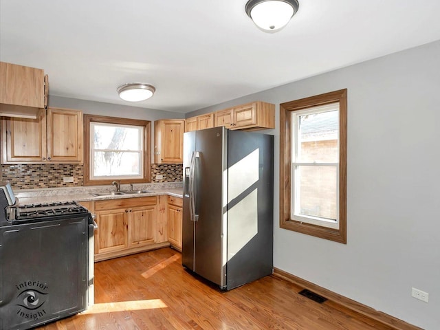 kitchen featuring light brown cabinetry, sink, stainless steel fridge, light hardwood / wood-style floors, and gas stove