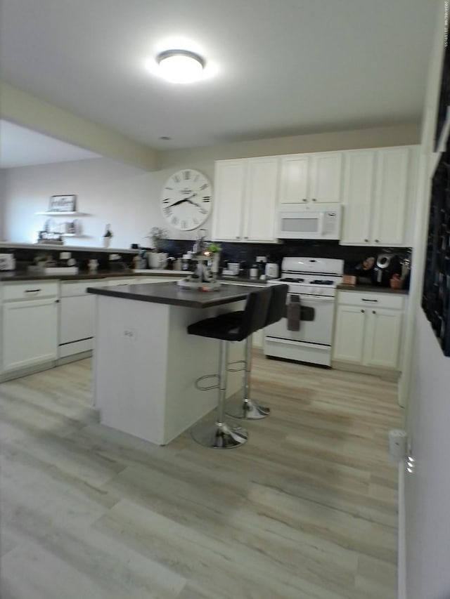 kitchen with a breakfast bar, a center island, light wood-type flooring, white appliances, and white cabinets