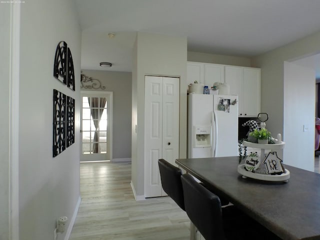 kitchen with white cabinetry, white refrigerator with ice dispenser, and light hardwood / wood-style flooring