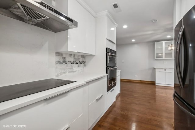 kitchen featuring black appliances, wall chimney range hood, light countertops, and white cabinetry