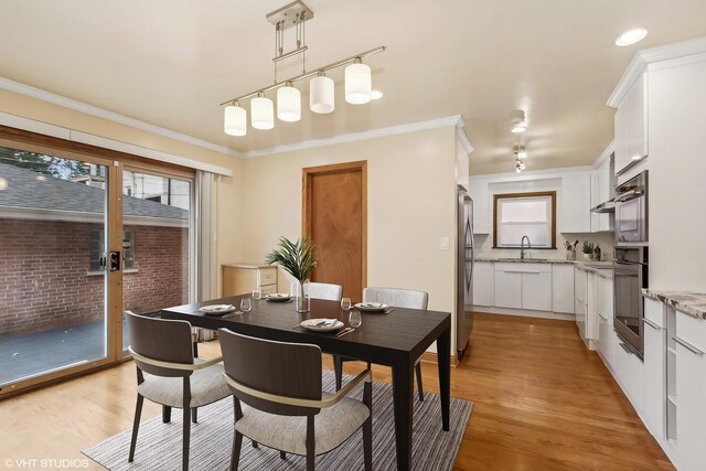 interior space with white cabinetry, ornamental molding, appliances with stainless steel finishes, pendant lighting, and light hardwood / wood-style floors