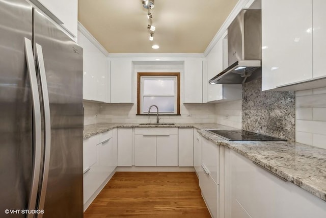 kitchen with freestanding refrigerator, white cabinets, a sink, wall chimney exhaust hood, and black electric cooktop