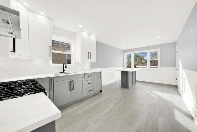 kitchen with sink, gray cabinetry, stainless steel appliances, light wood-type flooring, and wall chimney exhaust hood