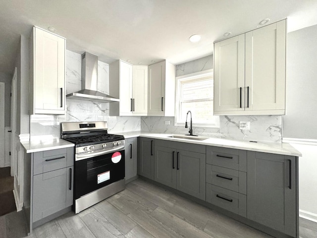 kitchen with sink, gray cabinetry, stainless steel range with gas stovetop, light hardwood / wood-style floors, and wall chimney range hood