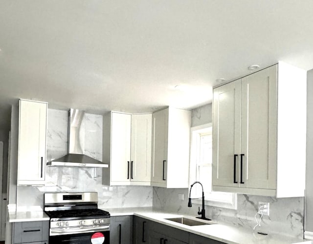 kitchen featuring sink, gas range, tasteful backsplash, wall chimney range hood, and white cabinets