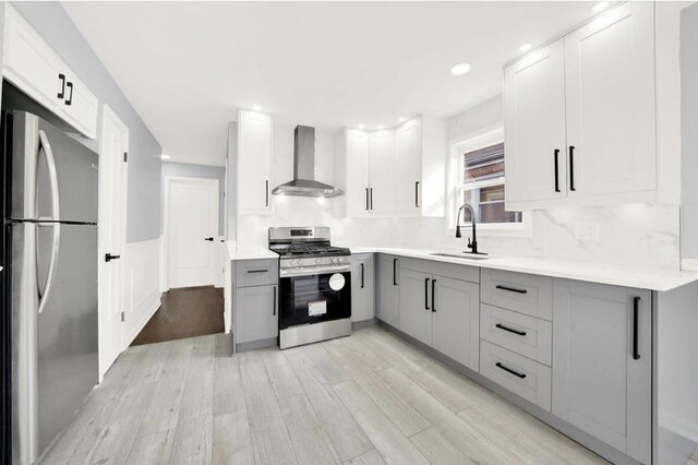 kitchen featuring gray cabinets, sink, white cabinets, stainless steel appliances, and wall chimney exhaust hood