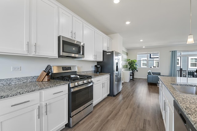 kitchen with light stone countertops, appliances with stainless steel finishes, white cabinets, and decorative light fixtures