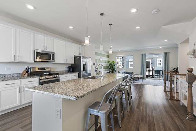 kitchen with appliances with stainless steel finishes, pendant lighting, an island with sink, sink, and white cabinets