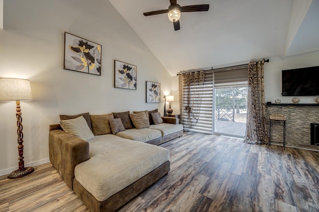 living room with ceiling fan, a stone fireplace, hardwood / wood-style floors, and high vaulted ceiling