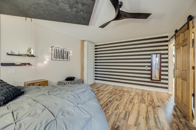 bedroom with wood-type flooring, a barn door, and ceiling fan