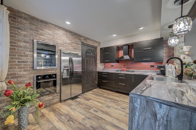 kitchen featuring sink, light wood-type flooring, appliances with stainless steel finishes, pendant lighting, and wall chimney range hood