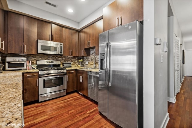 kitchen with sink, stainless steel appliances, dark hardwood / wood-style floors, light stone counters, and decorative backsplash