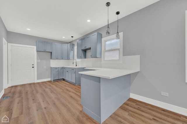 kitchen featuring sink, hanging light fixtures, decorative backsplash, kitchen peninsula, and light wood-type flooring