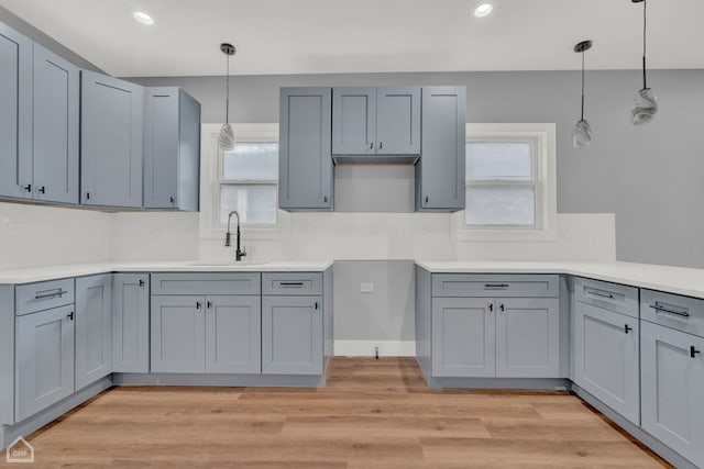 kitchen with sink, gray cabinetry, light wood-type flooring, and decorative light fixtures