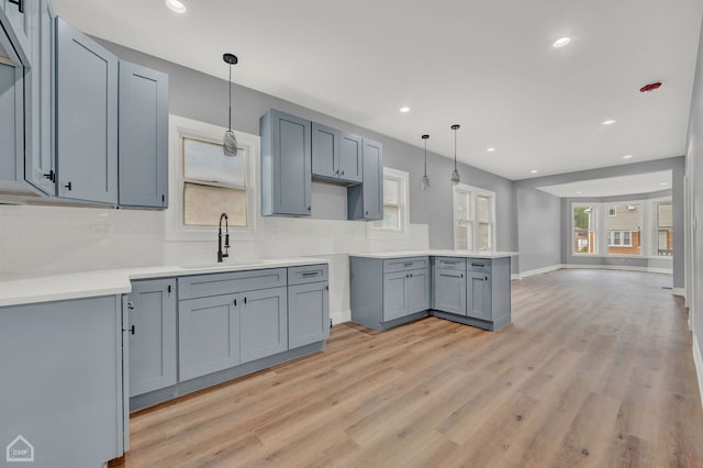 kitchen featuring sink, pendant lighting, backsplash, and light wood-type flooring