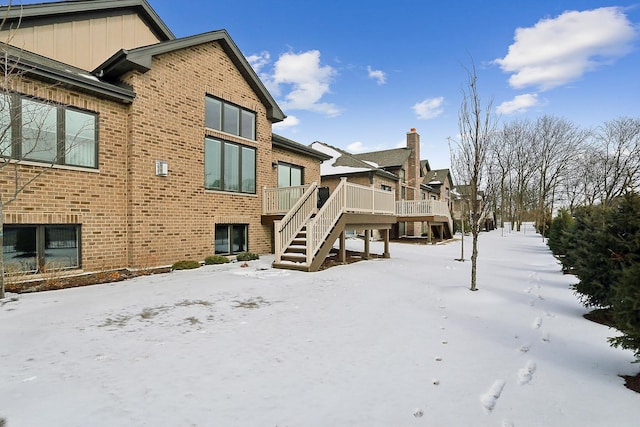 snow covered rear of property with stairs, brick siding, board and batten siding, and a deck