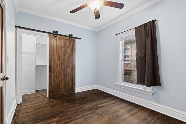 unfurnished bedroom with baseboards, a barn door, dark wood finished floors, and crown molding