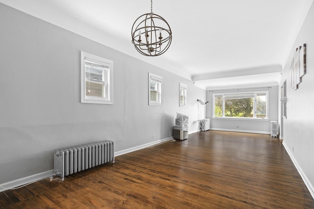 unfurnished living room with baseboards, dark wood-type flooring, an inviting chandelier, and radiator