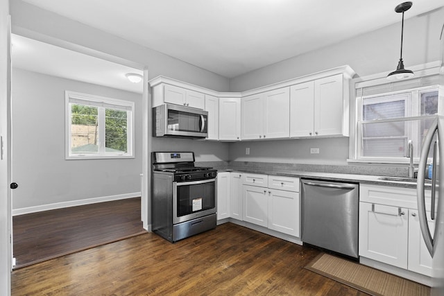 kitchen with appliances with stainless steel finishes, white cabinets, dark wood finished floors, and decorative light fixtures