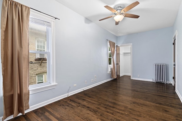 spare room featuring baseboards, dark wood finished floors, a ceiling fan, and radiator