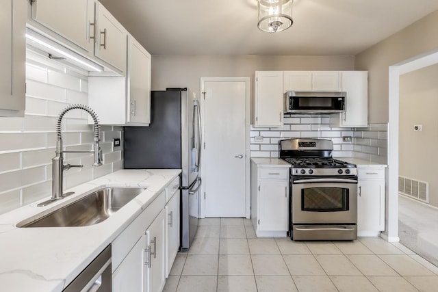 kitchen featuring sink, appliances with stainless steel finishes, tasteful backsplash, light stone countertops, and white cabinets