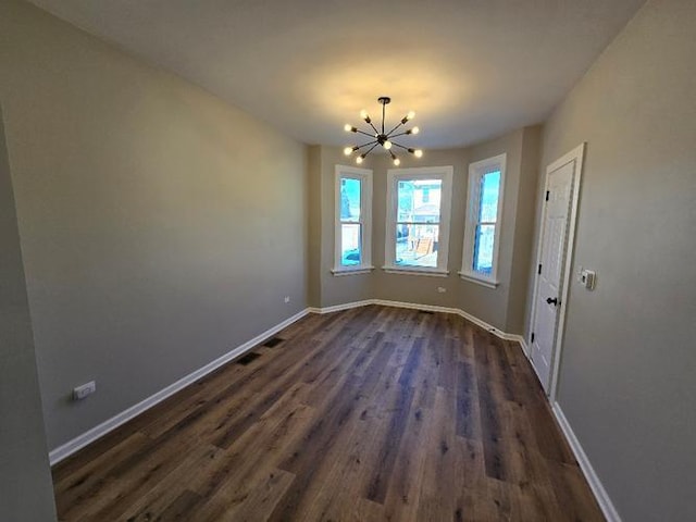 unfurnished dining area with a chandelier, dark wood finished floors, and baseboards