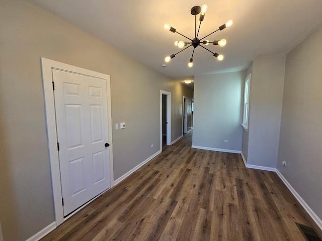 empty room with baseboards, wood finished floors, visible vents, and a notable chandelier