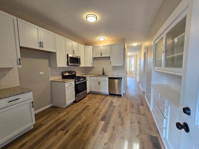 kitchen with white cabinets, light stone counters, wood finished floors, stainless steel appliances, and a sink