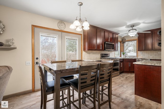 kitchen with light stone counters, light hardwood / wood-style flooring, appliances with stainless steel finishes, pendant lighting, and decorative backsplash