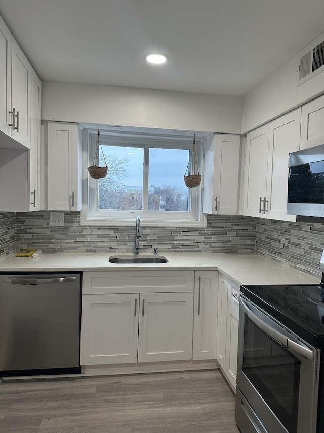 kitchen featuring sink, light hardwood / wood-style flooring, appliances with stainless steel finishes, white cabinets, and decorative backsplash