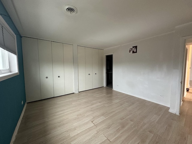 unfurnished bedroom featuring light hardwood / wood-style floors and two closets