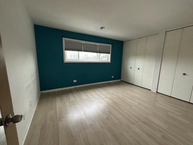 unfurnished bedroom featuring two closets and light wood-type flooring