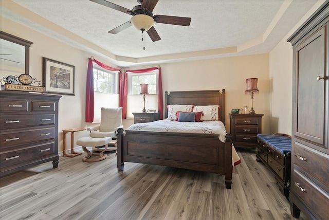 bedroom featuring ceiling fan, a textured ceiling, light hardwood / wood-style floors, and a tray ceiling