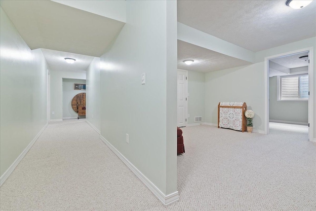 hallway with light carpet and a textured ceiling