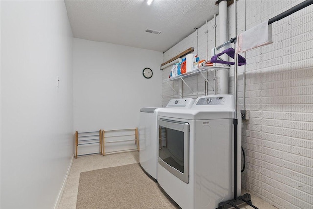 laundry area featuring washer and dryer, a textured ceiling, and brick wall