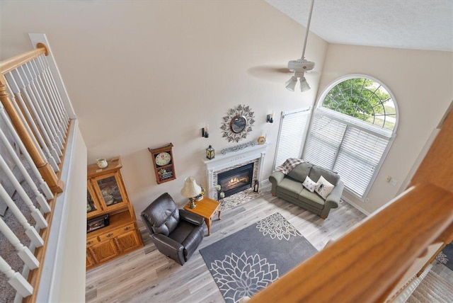 living room with ceiling fan, high vaulted ceiling, a textured ceiling, and light wood-type flooring