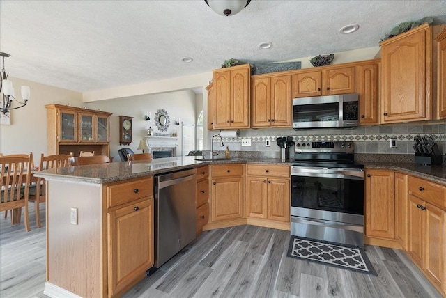 kitchen featuring sink, decorative light fixtures, light wood-type flooring, appliances with stainless steel finishes, and kitchen peninsula