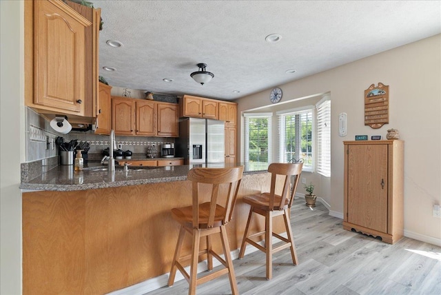 kitchen with light hardwood / wood-style flooring, a breakfast bar area, tasteful backsplash, stainless steel fridge with ice dispenser, and kitchen peninsula